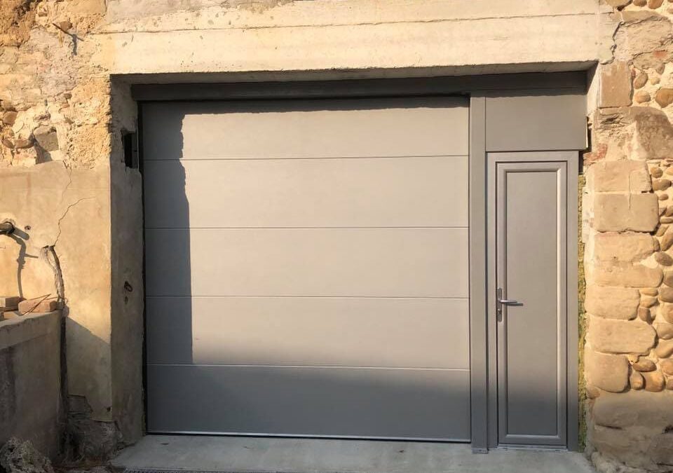 vue sur une porte de garage avec création d'une ossature acier pour installé une porte de service grise clair sur une façade pierre.Réalisation Rémy Ferere isère 38