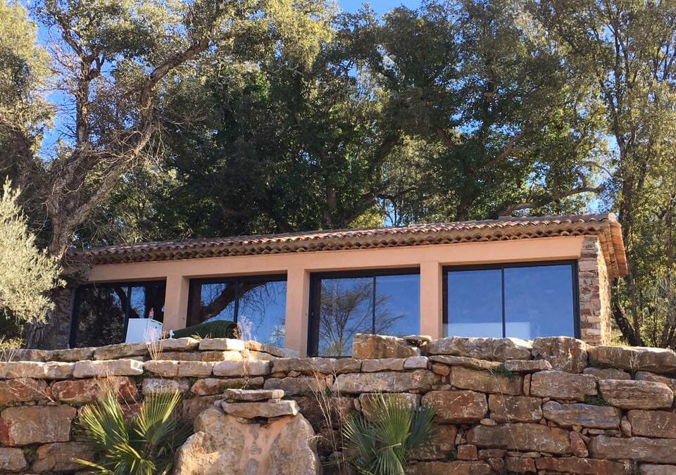 photo d'une terrasse fermée grâce à des coulissants aluminium, mur en pierre et petits palmiers.Réalisation Rémy Ferere cogelin 83