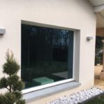 photo d'une facade de maison avec un fixe aluminium avec vitrage contrôle solaire, petit sapin à gauche. Réalisation Rémy Ferere st Vérand isere