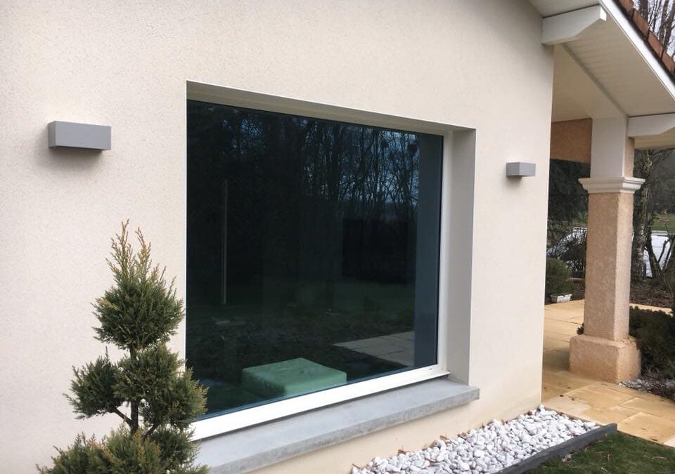 photo d'une facade de maison avec un fixe aluminium avec vitrage contrôle solaire, petit sapin à gauche. Réalisation Rémy Ferere st Vérand isere