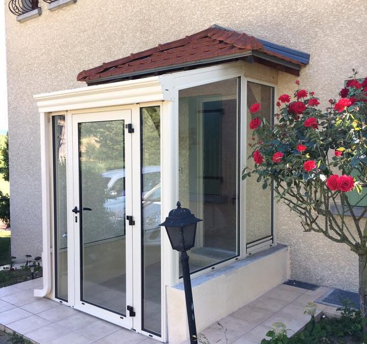 photo d'un sas d'entrée blanc en aluminium installé pour agrandir l'espace d'entrée, toit au tuile rouge qui protège de la pluie.