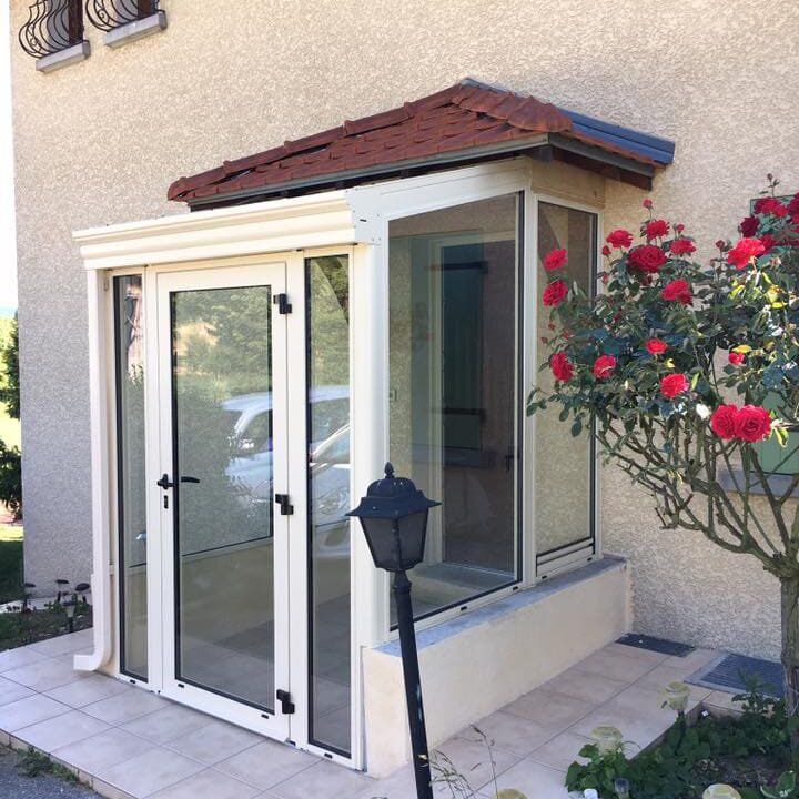 photo d'un sas d'entrée blanc en aluminium installé pour agrandir l'espace d'entrée, toit au tuile rouge qui protège de la pluie.