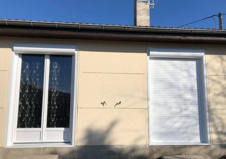 Une menuiserie blanche PVC 2 vantaux avec rideau et une autre au volet roulant blanc fermé sur la façade d'une maison.