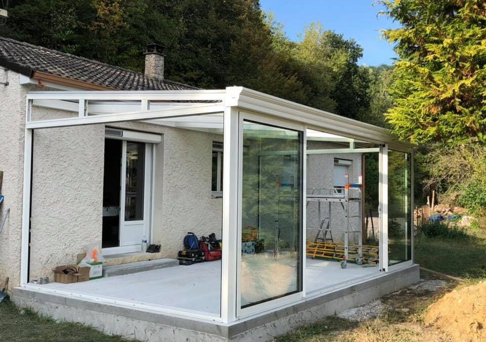 Construction d'une véranda vitrée PVC blanche avec échaufaudage sur la dalle et unbattant de porte fenêtre ouvert.